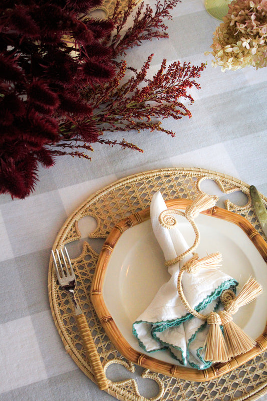 Decorative table setting with a woven charger, white plate, and decorative napkin on a checkered tablecloth.